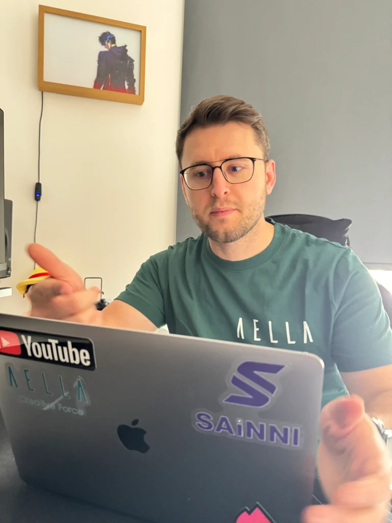 Briken Bufi wearing an Aella Creative Force t-shirt working on a laptop in a modern office.